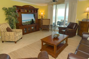 A living room with a television, leather sofas, a coffee table, and a view of the ocean through large windows.