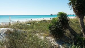 A beach with a wooden fence, palm trees, and a pier in the distance. - Heron L09-Stunning Corner Lanai Level Condo...Wrap around balcony (Fort Walton Beach)