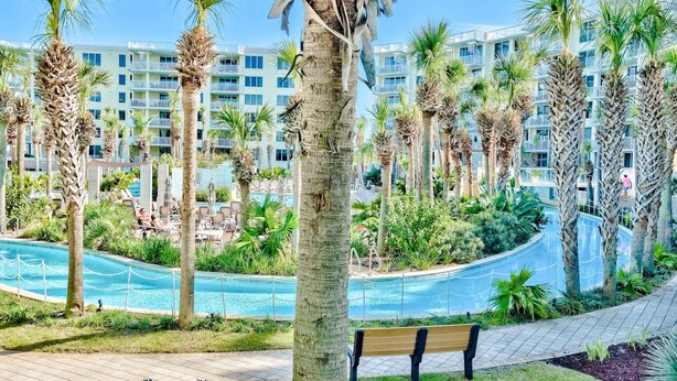A resort with a pool, palm trees, and a building with balconies. - Heron L09-Stunning Corner Lanai Level Condo...Wrap around balcony (Fort Walton Beach)