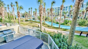 A poolside area with a grill, palm trees, and a view of a hotel building. - Heron L09-Stunning Corner Lanai Level Condo...Wrap around balcony (Fort Walton Beach)