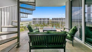 A balcony with a green cushioned sofa, a small table, and a spiral staircase.