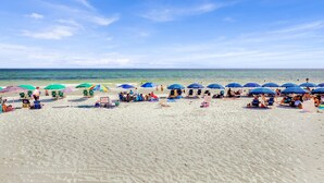 A beach with rows of umbrellas and beach chairs, a clear sky, and the ocean in the background.