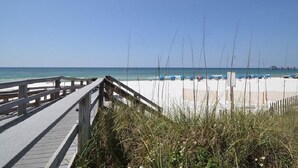 Une promenade en bois qui mène à une plage de sable blanc, sous un ciel bleu et dégagé.