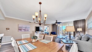 Een moderne woonkamer met een houten eettafel, witte stoelen, een grijze bank en een plafondventilator.