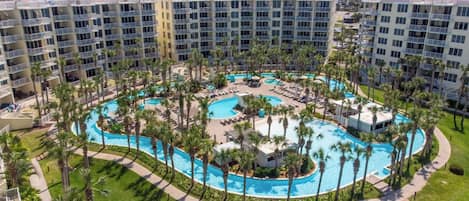 A hotel with multiple floors, a central pool area surrounded by palm trees, and a view of the ocean.