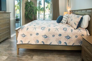 A bedroom with a bed featuring a sea-themed quilt, a wooden headboard, and a nightstand with a lamp.