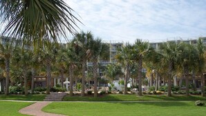 A hotel courtyard with a curved pathway, palm trees, and a building with balconies.