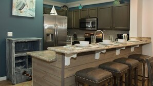 A kitchen with a central island, dark wooden cabinets, stainless steel appliances, and a nautical-themed wall art piece.