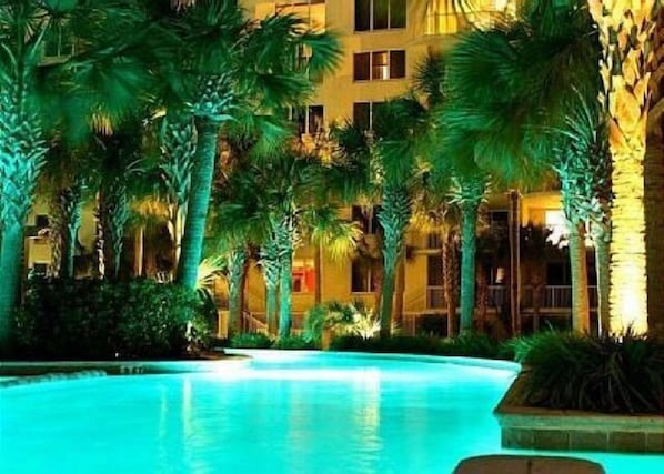 A pool surrounded by palm trees and a building with multiple windows.