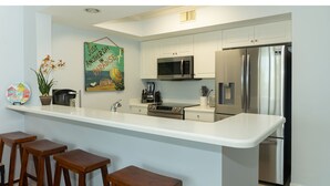 Una cocina moderna con una isla central, taburetes de bar, electrodomésticos de acero inoxidable y un cuadro decorativo en la pared.