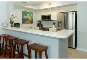A modern kitchen with a central island, bar stools, stainless steel appliances, and a decorative painting on the wall. - SANDPIPER 307 @DESTIN WEST-SLEEPS 7, BAYSIDE, LAZY RIVER AND BEACH ACCESS (Fort Walton Beach)
