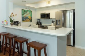 Cozinha moderna com ilha central, banquetas, eletrodomésticos de aço inoxidável e uma pintura decorativa na parede.