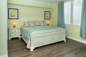 A bedroom with a large bed, two bedside tables, a nightstand, and a window with blinds.