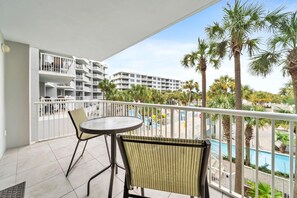 Un balcon avec une table ronde et deux chaises, donnant sur une piscine et des palmiers.