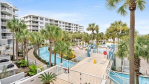 A hotel with multiple balconies, a swimming pool, and palm trees. - SANDPIPER 308-BAYSIDE CONDO @ DESTIN WEST SLEEPS 7 (Fort Walton Beach)