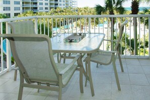 Ein Balkon mit einem Glastisch und zwei Stühlen, der auf einen Pool und ein Gebäude mit Balkonen blickt.