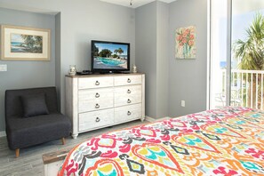 Ein Schlafzimmer mit Bett, Fernseher auf einer Kommode, einem grauen Sofa und einem Balkon mit Blick.