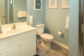 Ein Badezimmer mit weißem Waschbecken, WC und Waschtisch. An der Wand befinden sich gerahmte Bilder und ein Handtuchhalter.