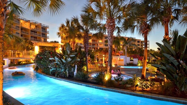 A swimming pool surrounded by palm trees and a building with multiple balconies. - Sandpiper 508-1 BR+Bunkroom Corner Condo with Amazing views of Lazy River and Gulf! (Fort Walton Beach)