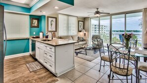 A modern kitchen with a central island, white cabinetry, and a view of the city through large windows. - Sandpiper 508-1 BR+Bunkroom Corner Condo with Amazing views of Lazy River and Gulf! (Fort Walton Beach)