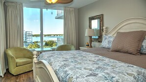 Habitación de hotel con una cama grande, una silla, una mesita de noche y vistas al mar.