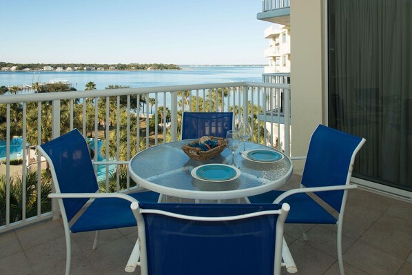 Un balcon avec une table ronde, des chaises bleues et une vue sur une étendue d’eau et des bâtiments au loin.