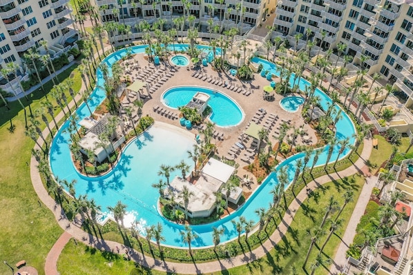 An aerial view of a hotel with multiple swimming pools, palm trees, and sun loungers.