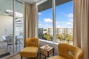 Relax on the balcony with a glass door leading to an outdoor seating area, featuring two armchairs and a side table.