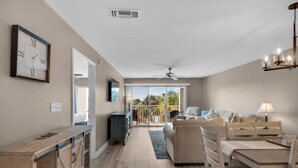 A spacious living area with a sofa, dining table, and chairs. There is a large window providing a view of the outdoors.