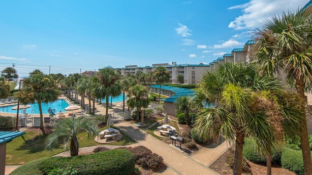 A resort with a swimming pool, palm trees, and a covered patio area.
