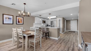 A modern kitchen with white cabinets, a stainless steel refrigerator, and a dining area with wooden chairs and a table.