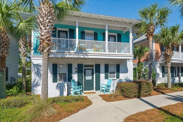 A two-story house with a balcony, a porch with chairs, and a well-maintained garden. - BUNGALOWS @ SEAGROVE! Near the Beach!!  Community Pool!! (Santa Rosa Beach)