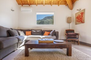 Ein Wohnzimmer mit einem dunkelbraunen Sofa, einem Holztisch und Blick auf eine Hügellandschaft durch ein Fenster.