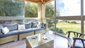 A modern living room with a large glass window, wicker sofa, and a glass coffee table. - Villa 4ch an idyllic haven of peace (Figari)