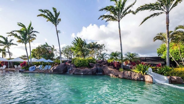 A pool area with clear water, palm trees, and lounge chairs. - Pili Mai 5L - 4 Bedroom Suite in Poipu Sleeps 8 AC, Pool, Fitness Center & More! (POIPU)