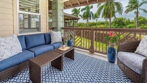 A covered balcony with a blue sofa, wicker furniture, and a patterned rug. - Pili Mai 5L - 4 Bedroom Suite in Poipu Sleeps 8 AC, Pool, Fitness Center & More! (POIPU)