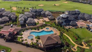 A residential area with multiple houses, a swimming pool, and a golf course in the background. - Pili Mai 5L - 4 Bedroom Suite in Poipu Sleeps 8 AC, Pool, Fitness Center & More! (POIPU)