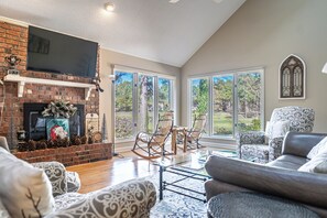 A living room with a fireplace, a television, and a large window offering a view of the outdoors. - Unwind at Cathedral Cottage: The Perfect Escape (Pinehurst)