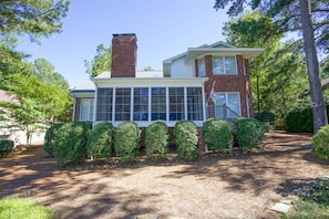 A two-story house with a brick chimney, a large front window, and a well-maintained garden with trimmed bushes. - Unwind at Cathedral Cottage: The Perfect Escape (Pinehurst)