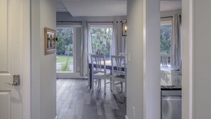 Eine moderne Küche mit Geschirrspüler, ein Essbereich mit Tisch und Stühlen sowie ein Blick ins Freie durch große Fenster.