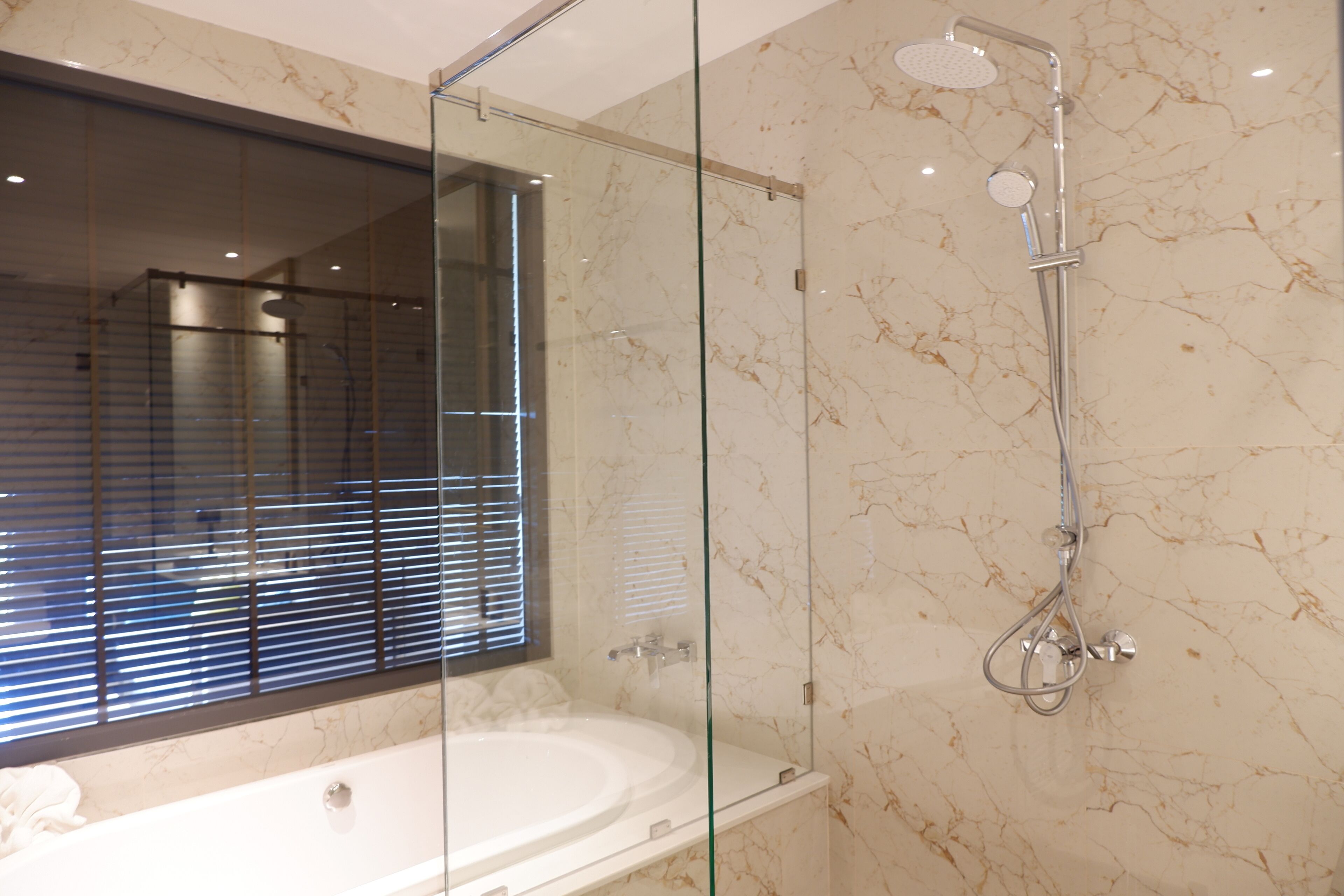 Ein modernes Badezimmer mit einer Glaskabine zur Dusche, einer großzügigen Badewanne und einer Marmorwand.
