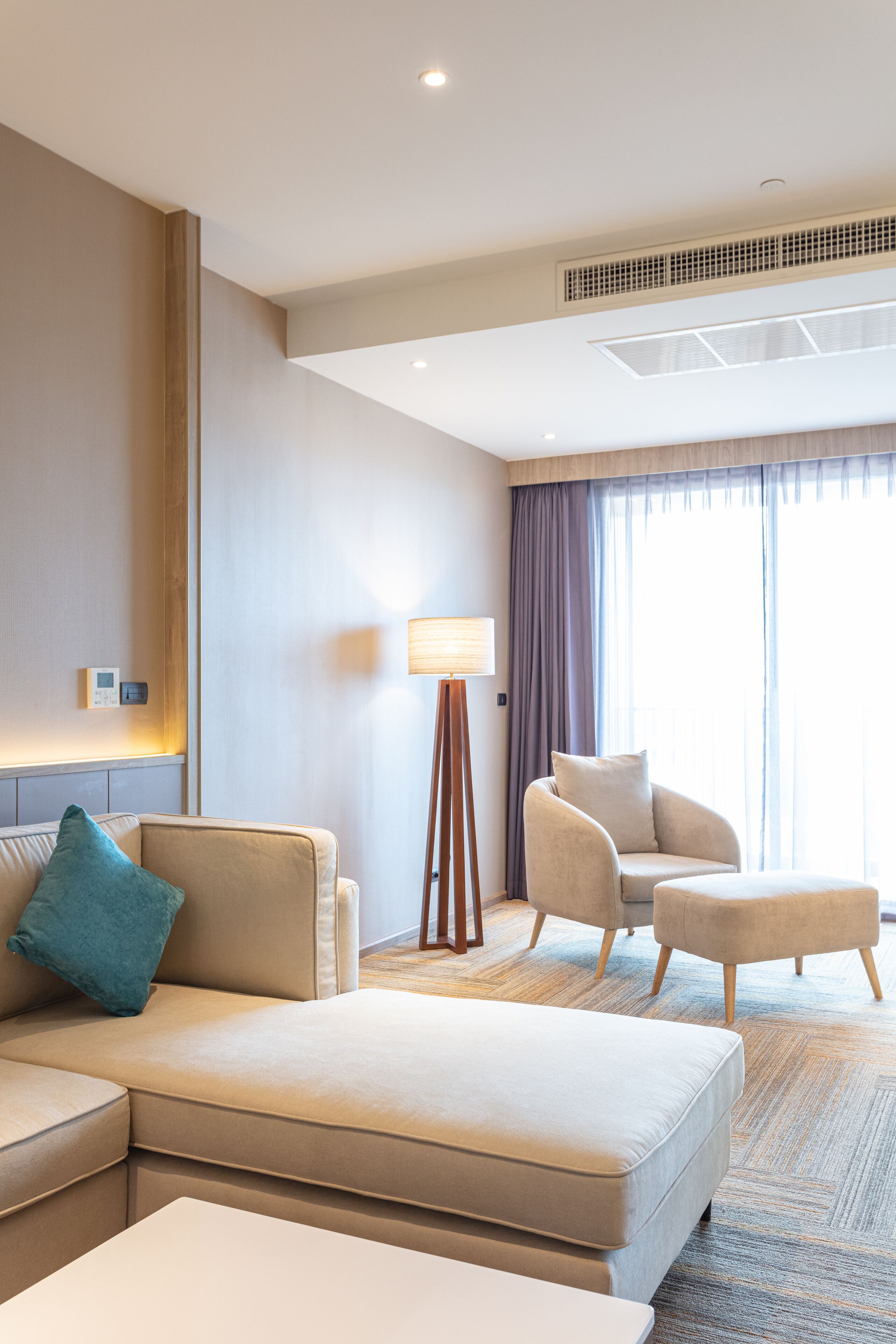 A modern hotel room with a sofa, armchair, ottoman, and a standing lamp.