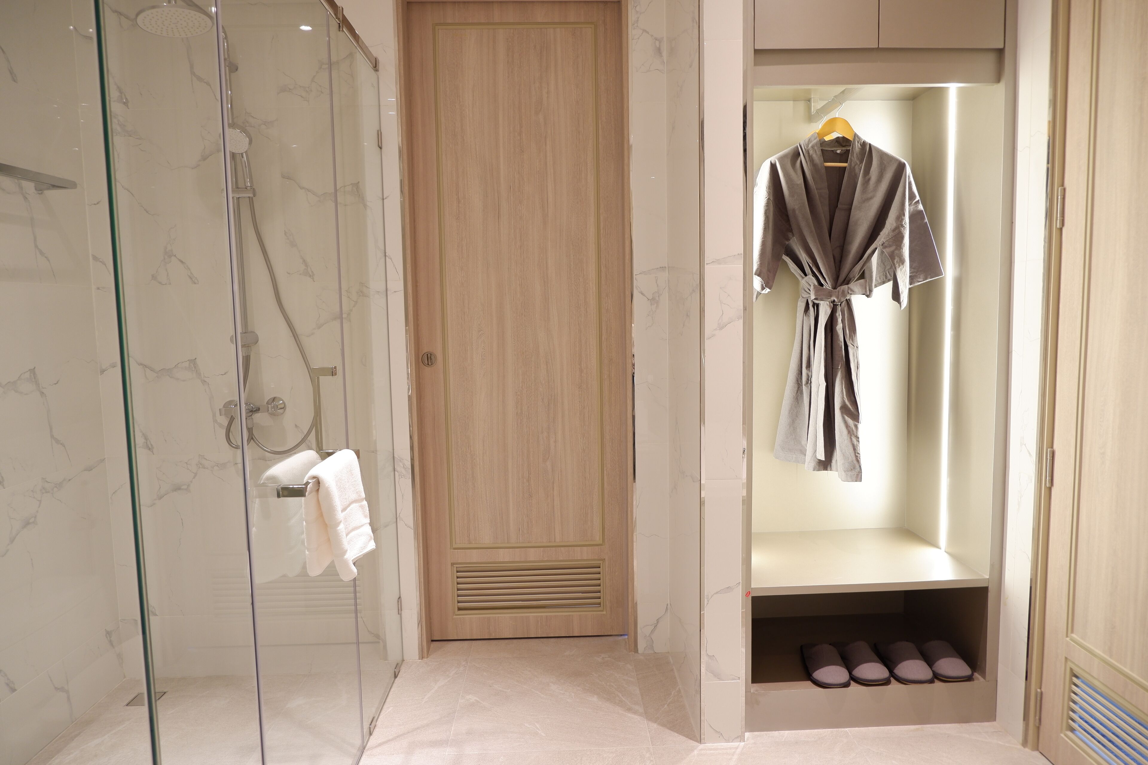 A modern bathroom with a glass shower enclosure, a wooden door, and a robe hanging on a rack.