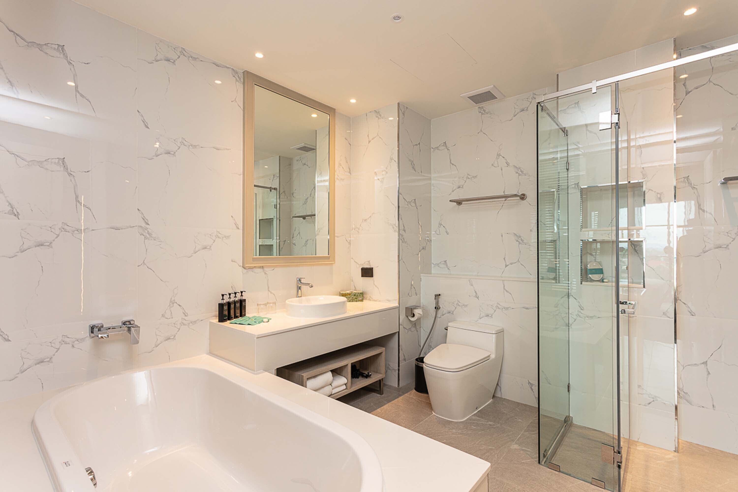 A modern bathroom with a large bathtub, a glass-enclosed shower, and a marble-tiled wall.