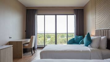 Een hotelkamer met een groot bed, een bureau en uitzicht op een groen landschap door het raam.