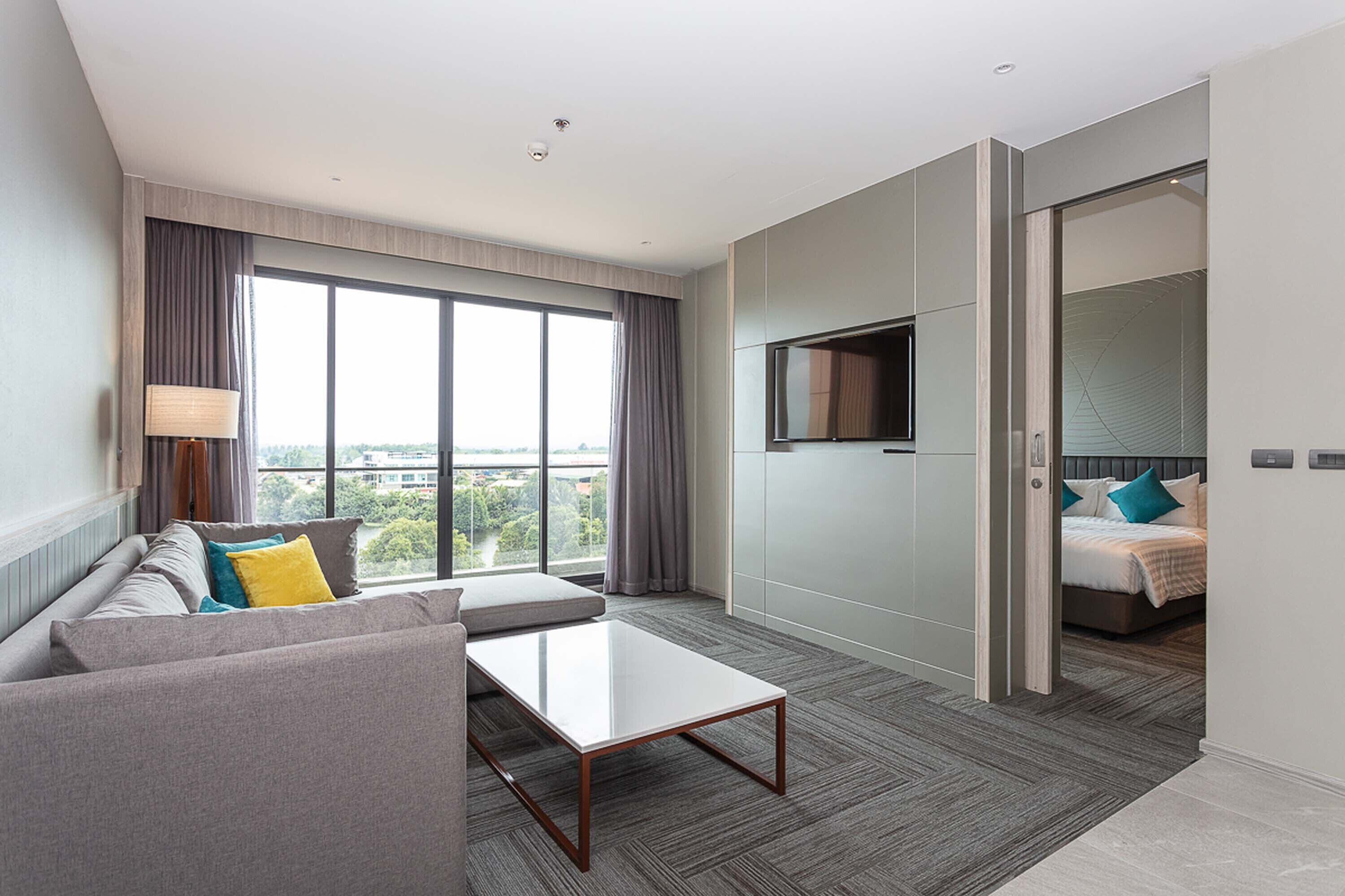 A modern hotel room with a sofa, a coffee table, a TV, and a bed with a view of the city.