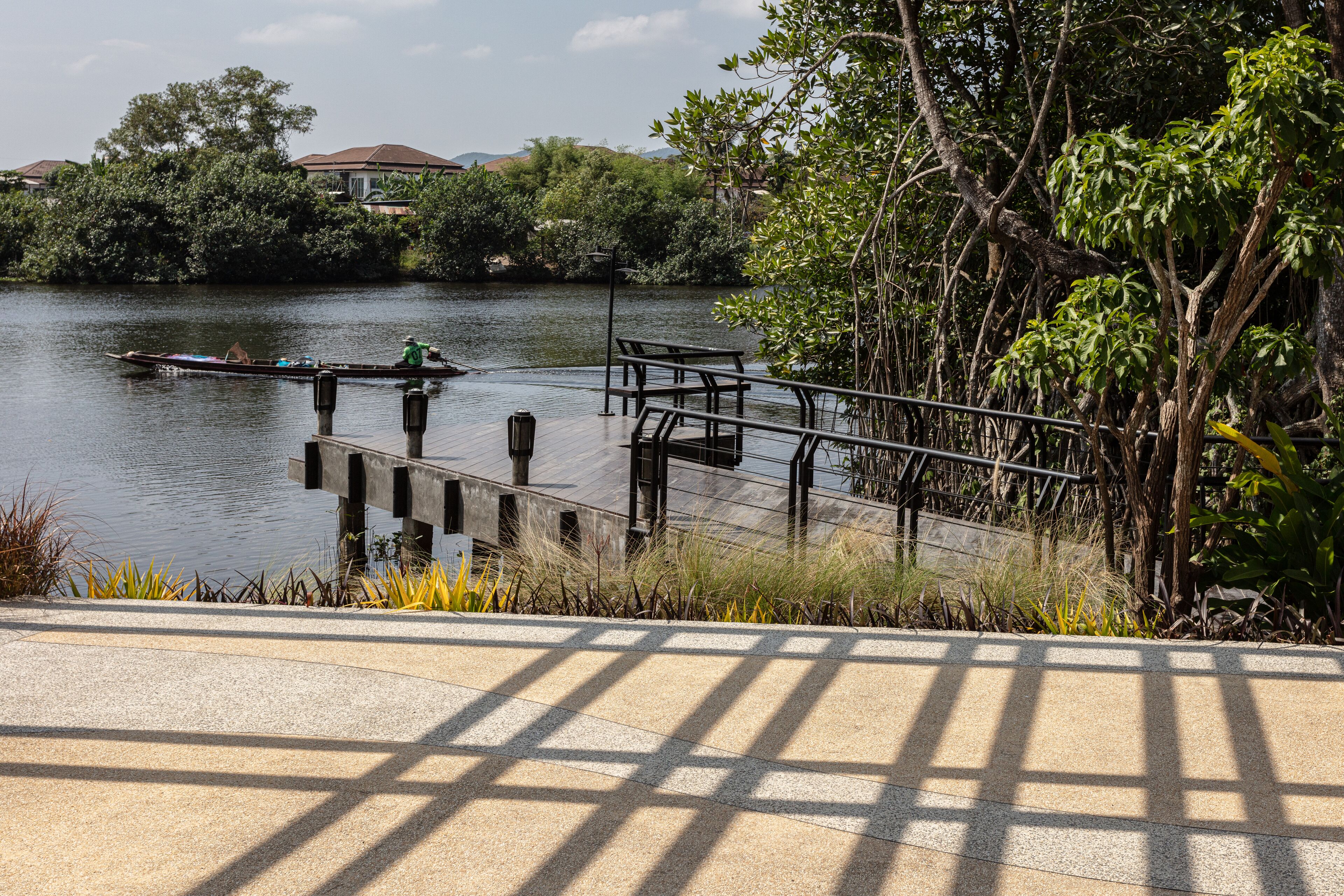 A riverside walkway with a dock, benches, and a boat.