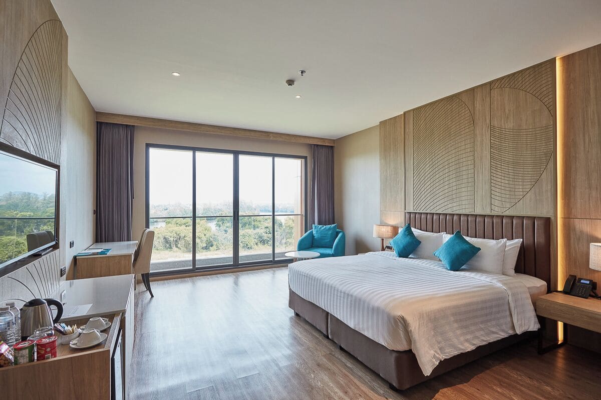 Habitación de hotel moderna con una cama grande, un escritorio con silla, una mesita y vistas al exterior a través de amplios ventanales.
