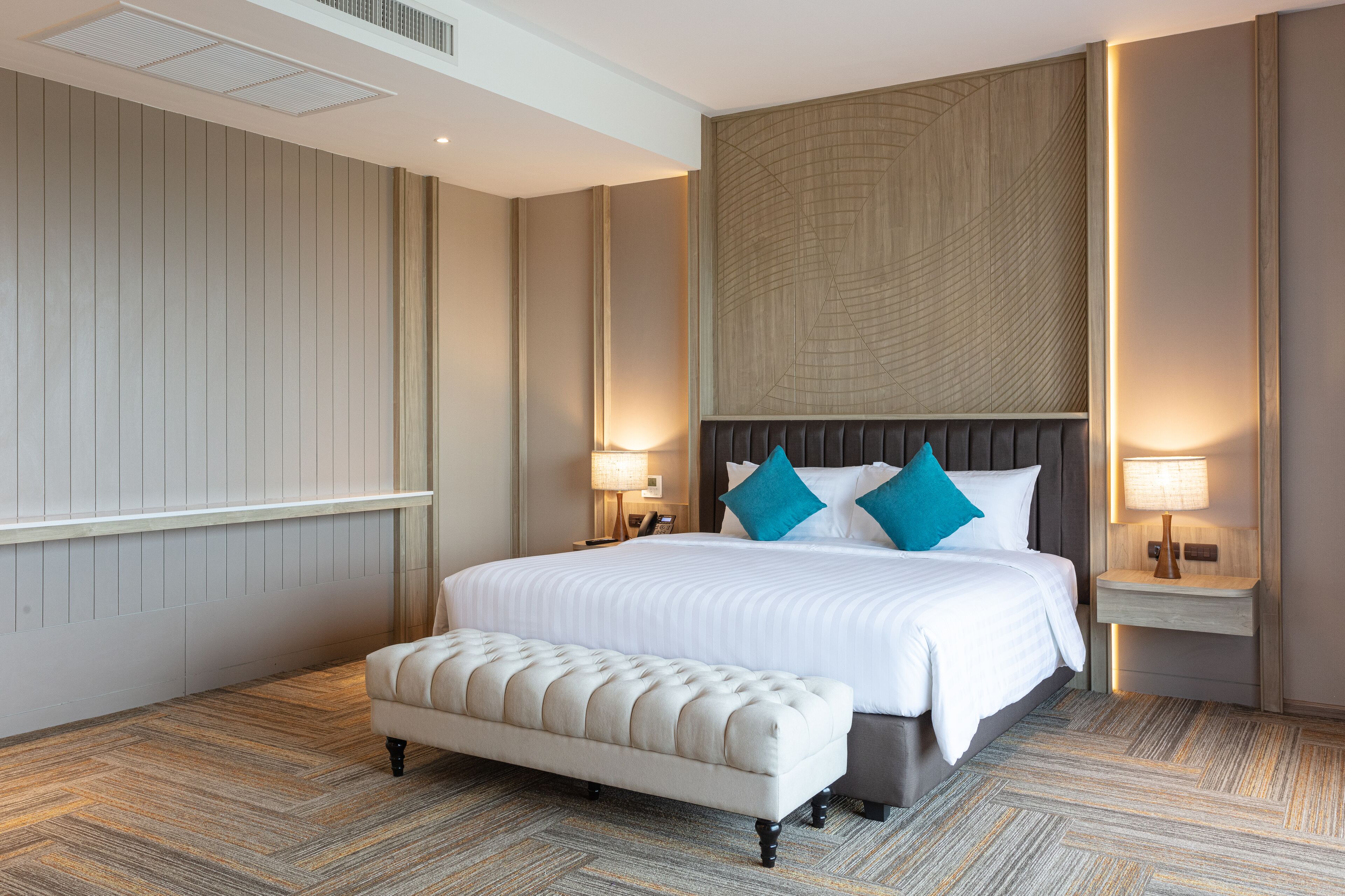 Een hotelkamer met een groot bed, een bankje, twee nachtkastjes met lampen en een decoratief wandpaneel.