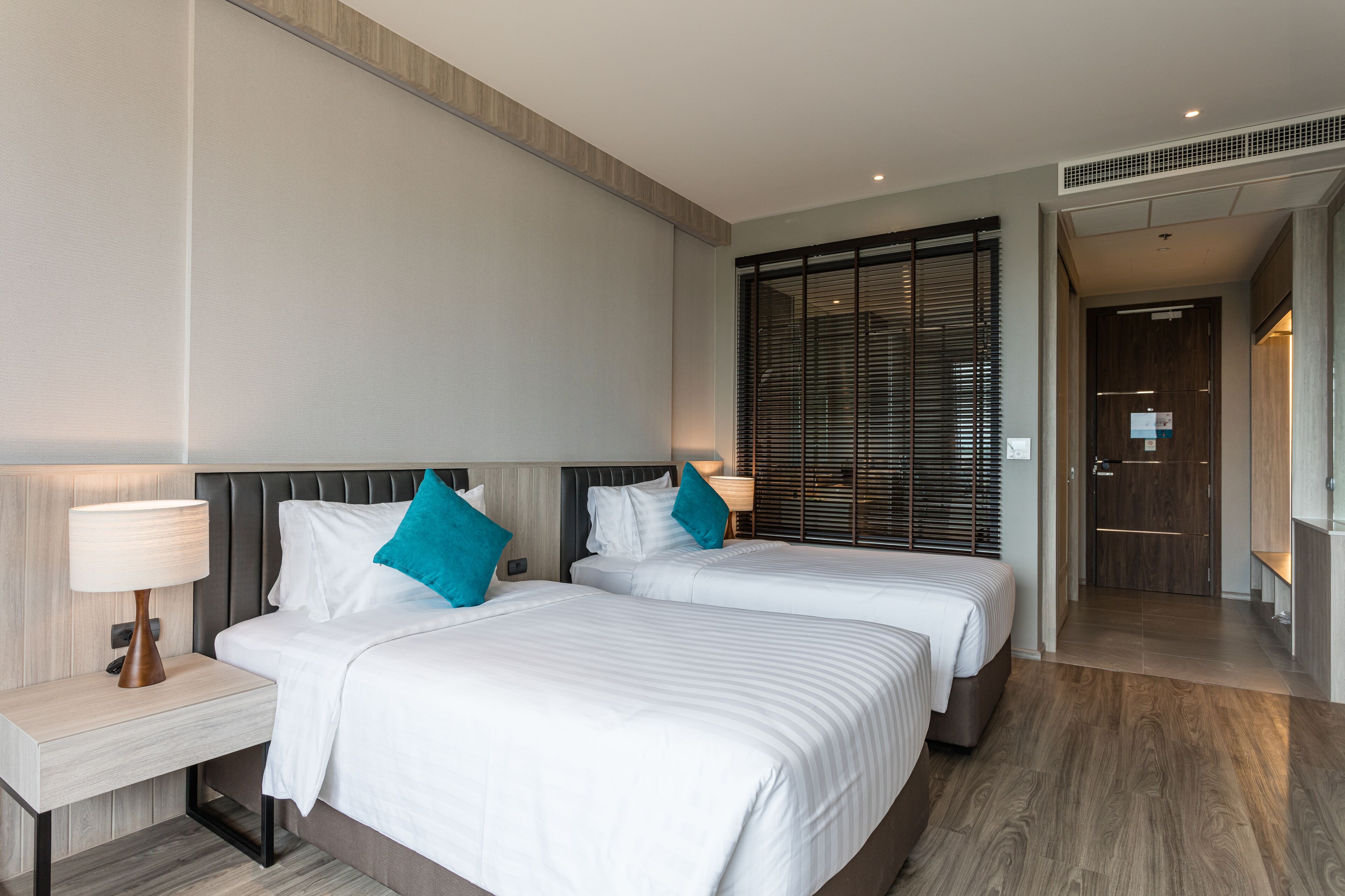 Habitación de hotel con dos camas, una mesita de noche, una lámpara fijada a la pared y una puerta corredera que da al baño.